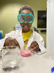 Little girl wearing lab coat and goggles doing science experiment at Boys & Girls Club